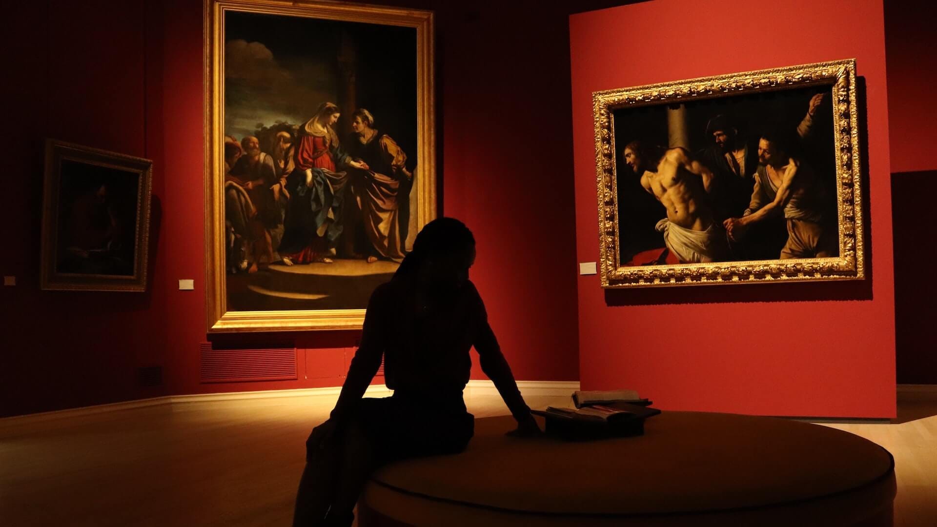 Silhouette of a woman sitting in a museum in front of images of Christ